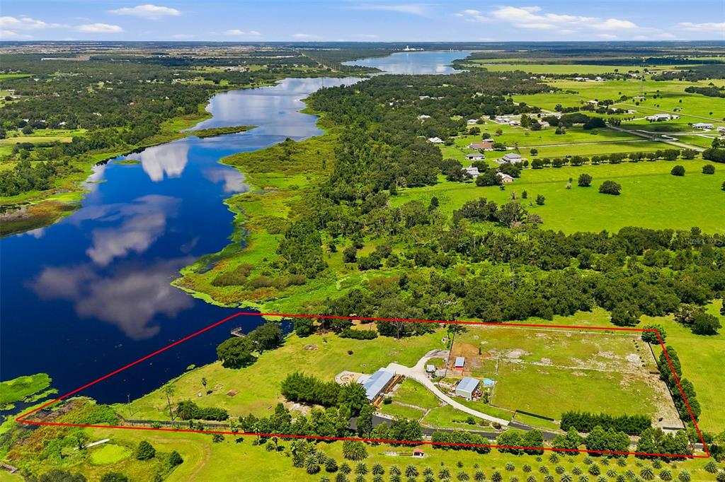 An aerial view shows a house and outbuildings on a waterfront lot with red boundary lines — 25916 STATE ROAD 64 E, MYAKKA CITY, FL