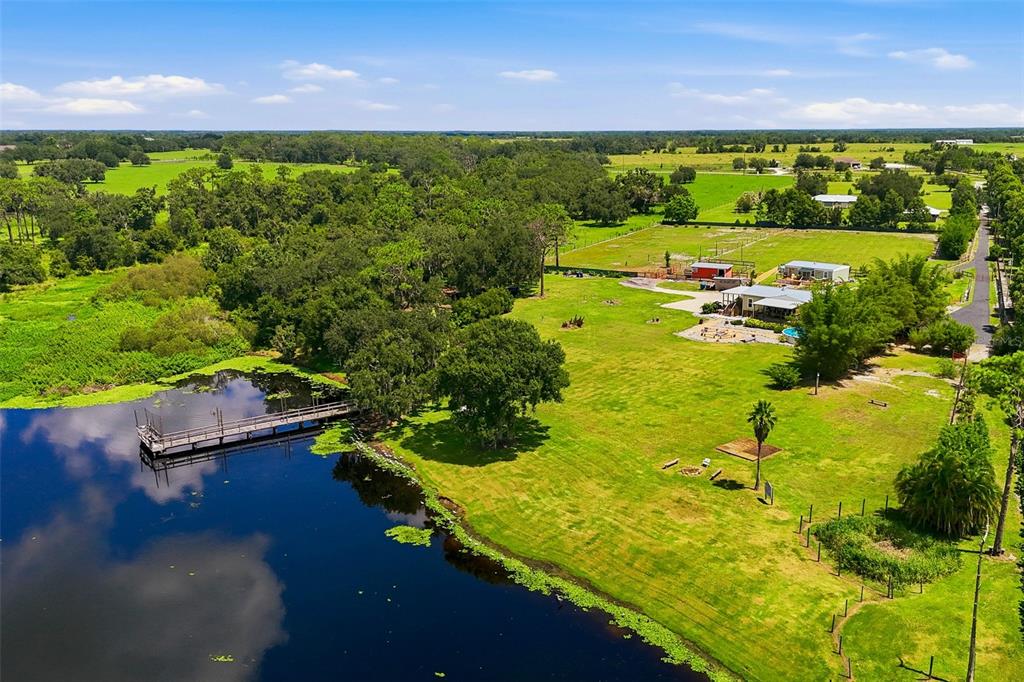 An aerial view shows a house with a dock on a lake and surrounding pasture — 25916 STATE ROAD 64 E, MYAKKA CITY, FL