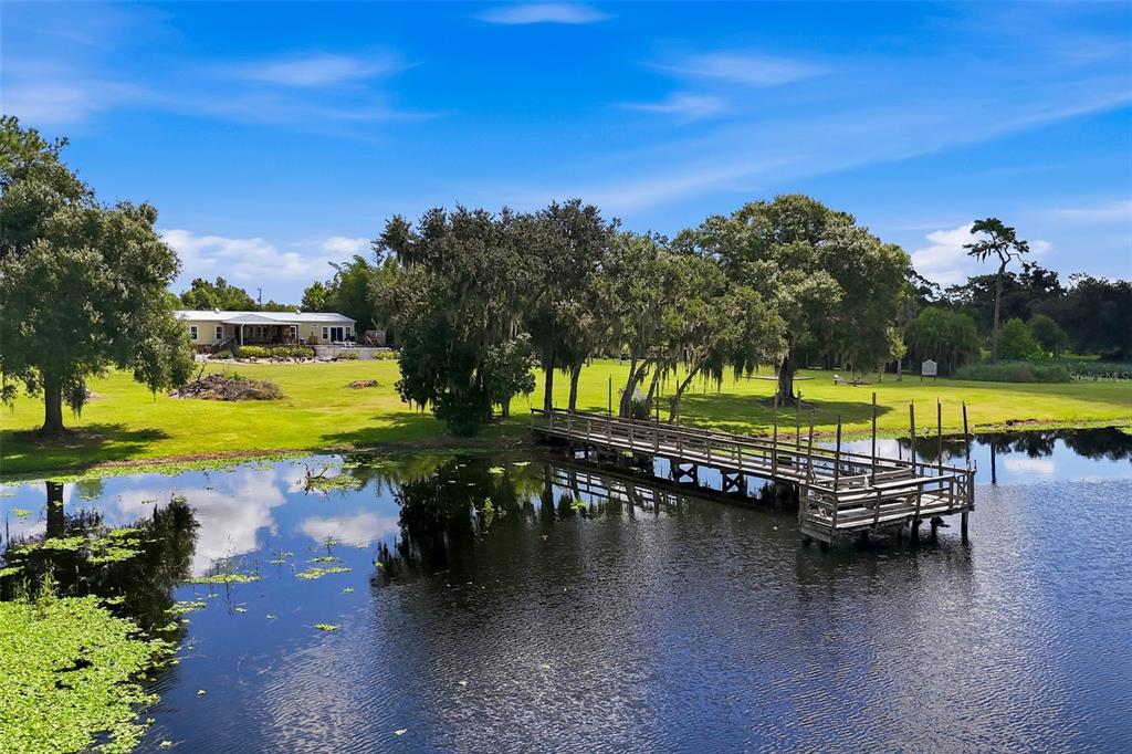 A wooden dock extends into a pond in front of a house on a lawn — 25916 STATE ROAD 64 E, MYAKKA CITY, FL