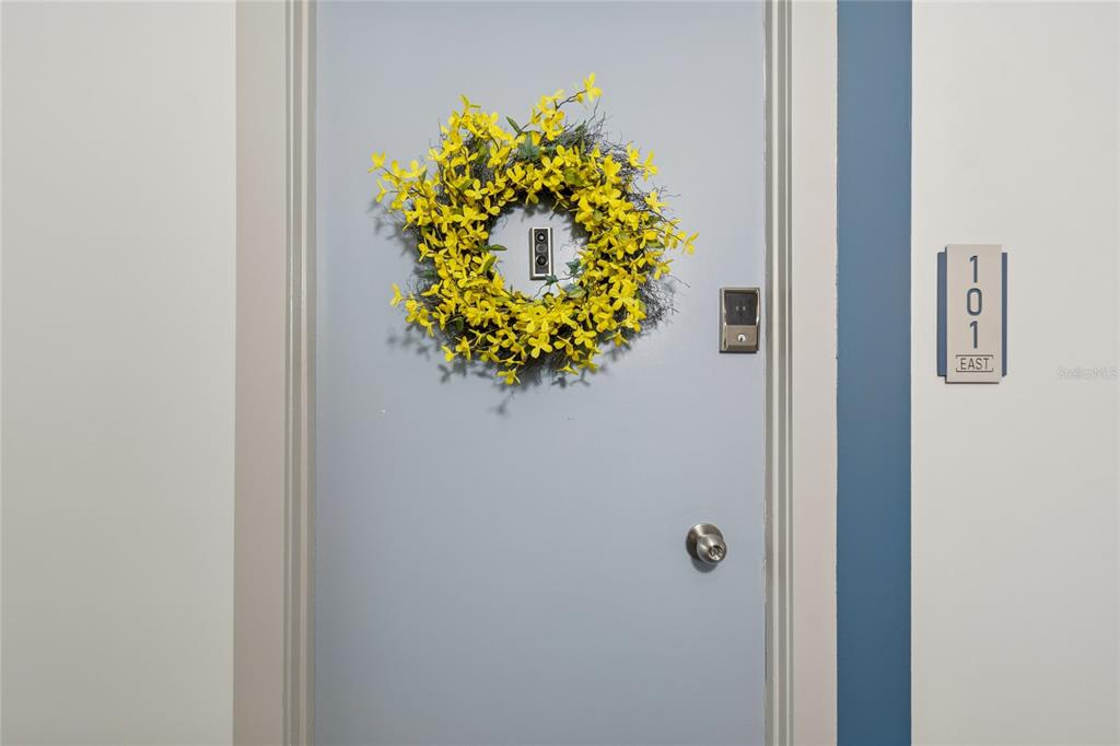 A light blue apartment door with a yellow wreath and a unit number sign — 1 KEY CAPRI UNIT 101E, TREASURE ISLAND, FL