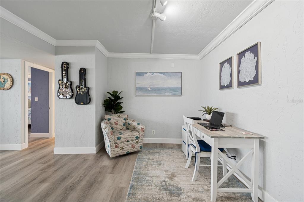 A home office features a desk, a patterned armchair, wall art, and light wood flooring — 1 KEY CAPRI UNIT 101E, TREASURE ISLAND, FL
