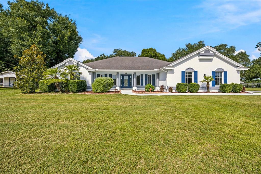 A white single-story house with blue shutters and a large front lawn — 16050 NW 10TH CIRCLE, CITRA, FL