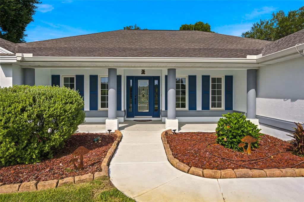 The front exterior of a single-story house features a blue door, columns, and landscaping — 16050 NW 10TH CIRCLE, CITRA, FL