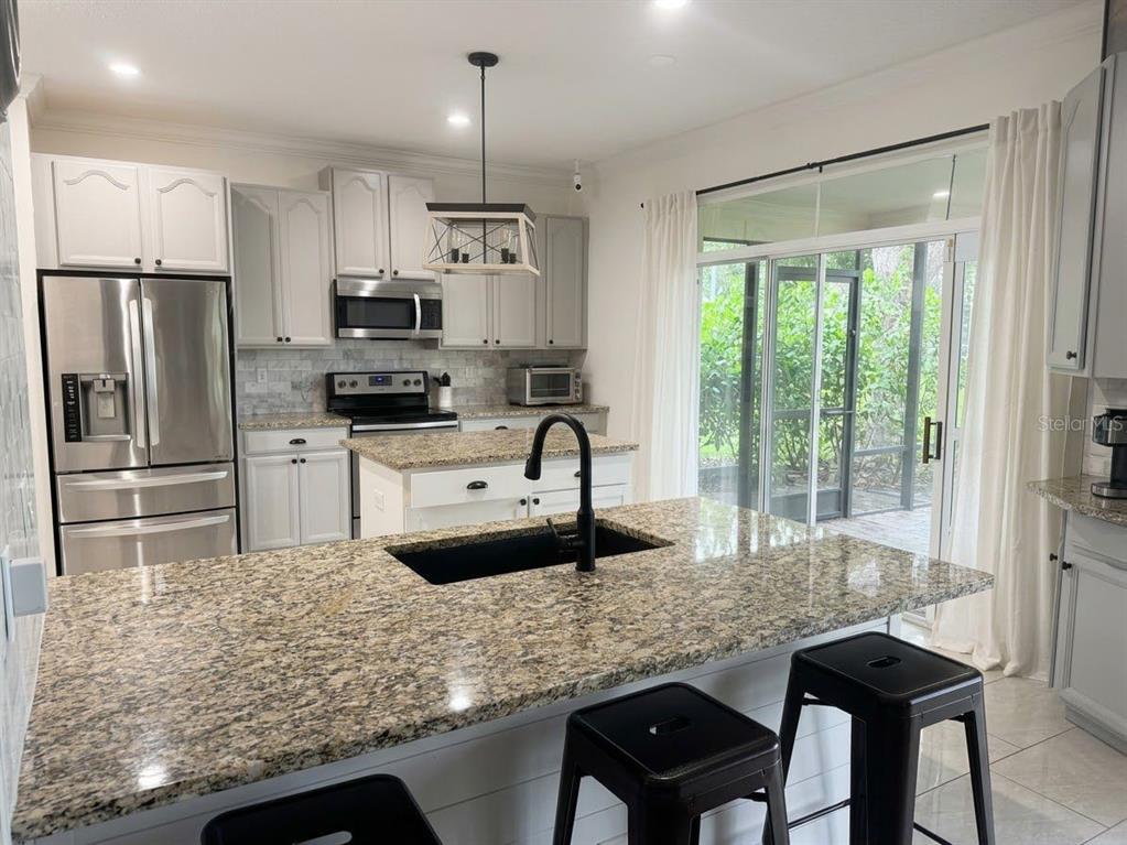 A kitchen with granite countertops, white cabinets, a central island, and a sliding glass door — 389 LAKEPARK TRAIL, OVIEDO, FL