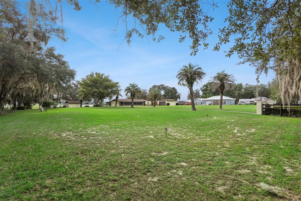 A wide, grassy lawn features several palm trees and mature oaks under a clear sky — 10617 SE 95TH TERRACE, BELLEVIEW, FL