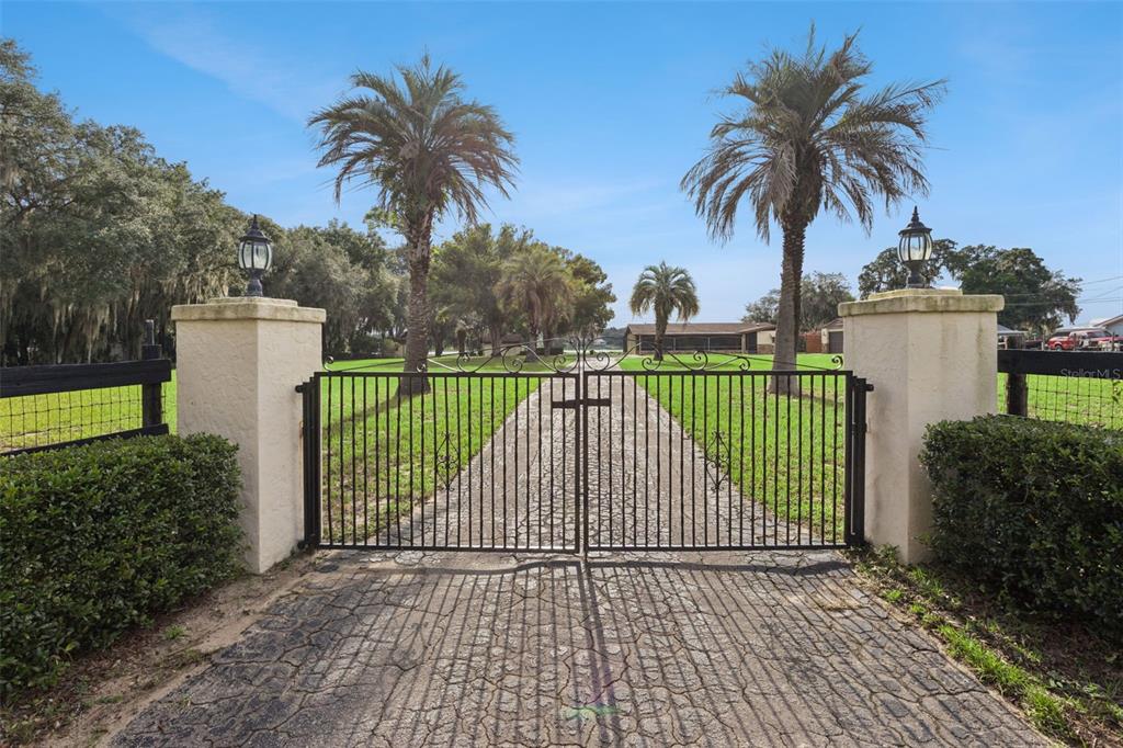 A black metal gate stands between two stucco pillars at the entrance to a driveway — 10617 SE 95TH TERRACE, BELLEVIEW, FL