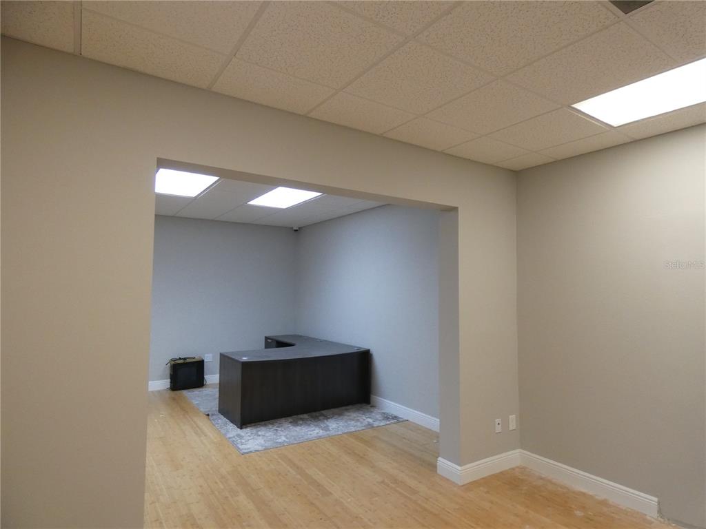 An office space features a dark L-shaped desk, light wood flooring, and a drop ceiling — 1882 PORTER LAKE DRIVE UNIT 106, SARASOTA, FL