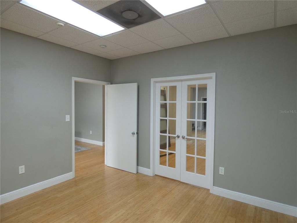 An empty room features gray walls, light wood flooring, a drop ceiling, and French doors — 1882 PORTER LAKE DRIVE UNIT 106, SARASOTA, FL