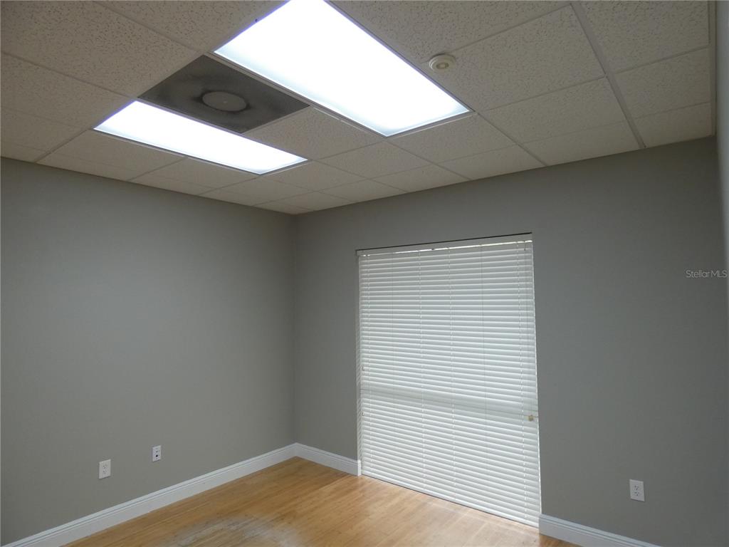 An empty office with gray walls, wood flooring, a drop ceiling, and a window with blinds — 1882 PORTER LAKE DRIVE UNIT 106, SARASOTA, FL