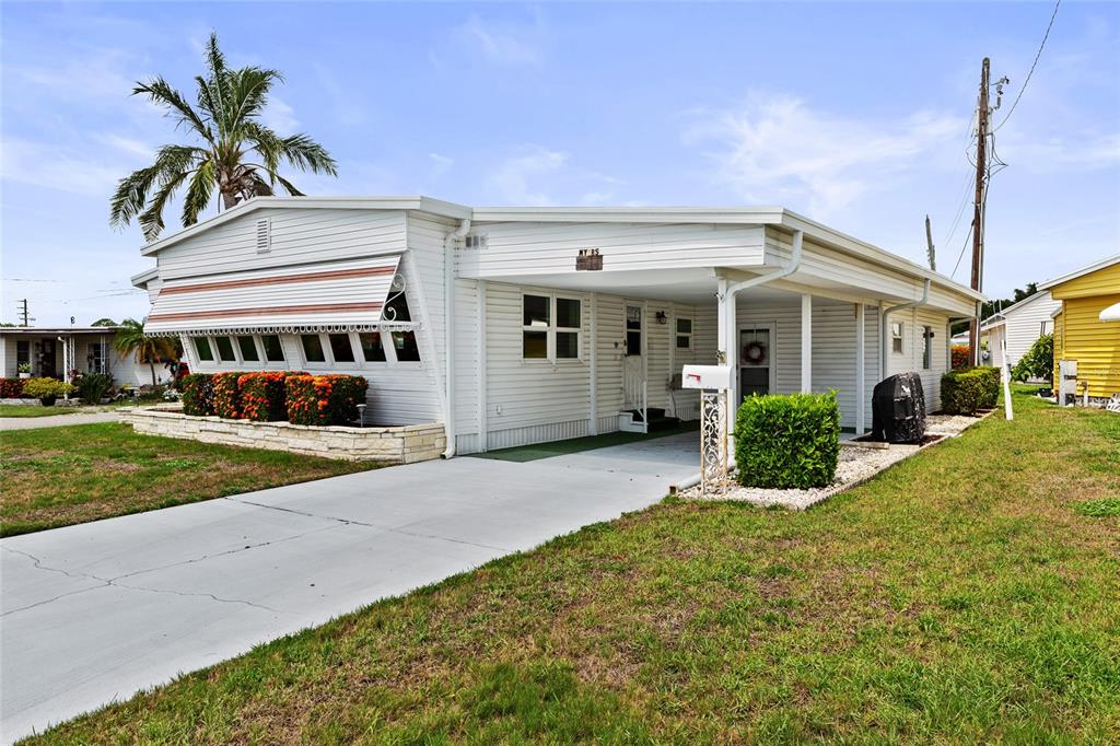 A white manufactured home features a stone retaining wall, green steps, and striped window awnings — 1111 42ND AVENUE E, ELLENTON, FL