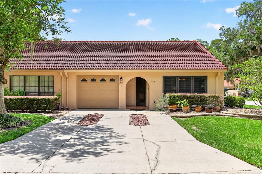 A single-story house with a tan stucco exterior, a red tile roof, and a concrete driveway — 1822 SW 34TH COURT, OCALA, FL
