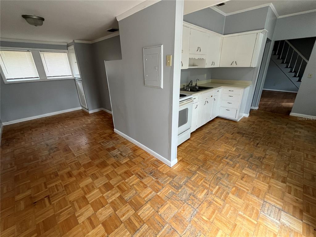 A kitchen with white cabinets and parquet wood flooring opens to a dining area — 403 8TH STREET NE, WINTER HAVEN, FL