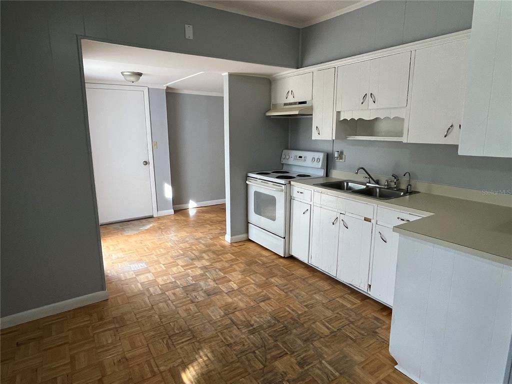 A kitchen features white cabinets, a white stove, a double sink, and parquet wood flooring — 403 8TH STREET NE, WINTER HAVEN, FL