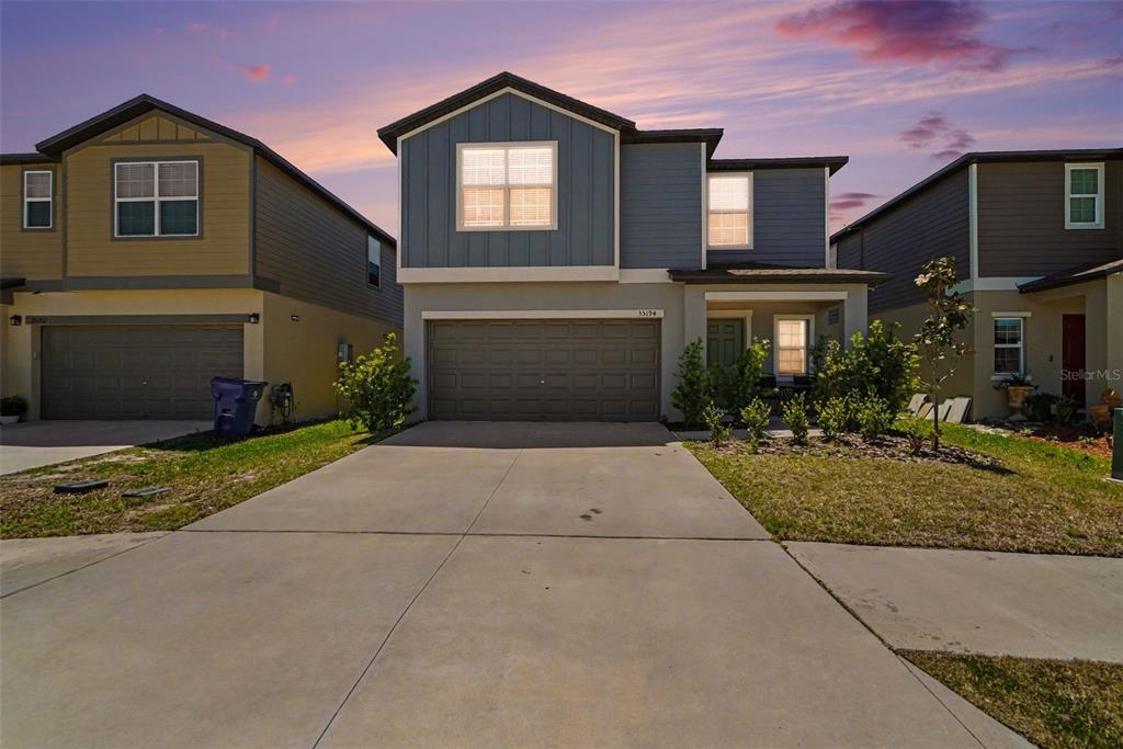 A two-story suburban house with a concrete driveway, a two-car garage, and blue siding — 35194 ACKLEY TRCE, ZEPHYRHILLS, FL