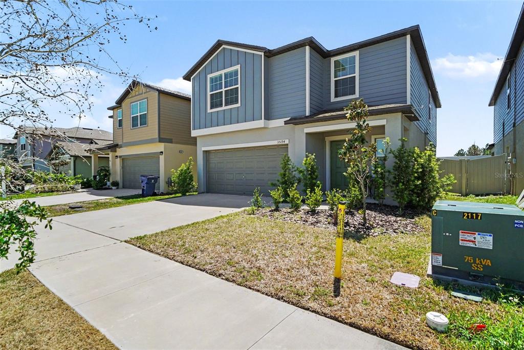 A two-story house with a blue-grey exterior, a two-car garage, and a green electrical transformer — 35194 ACKLEY TRCE, ZEPHYRHILLS, FL
