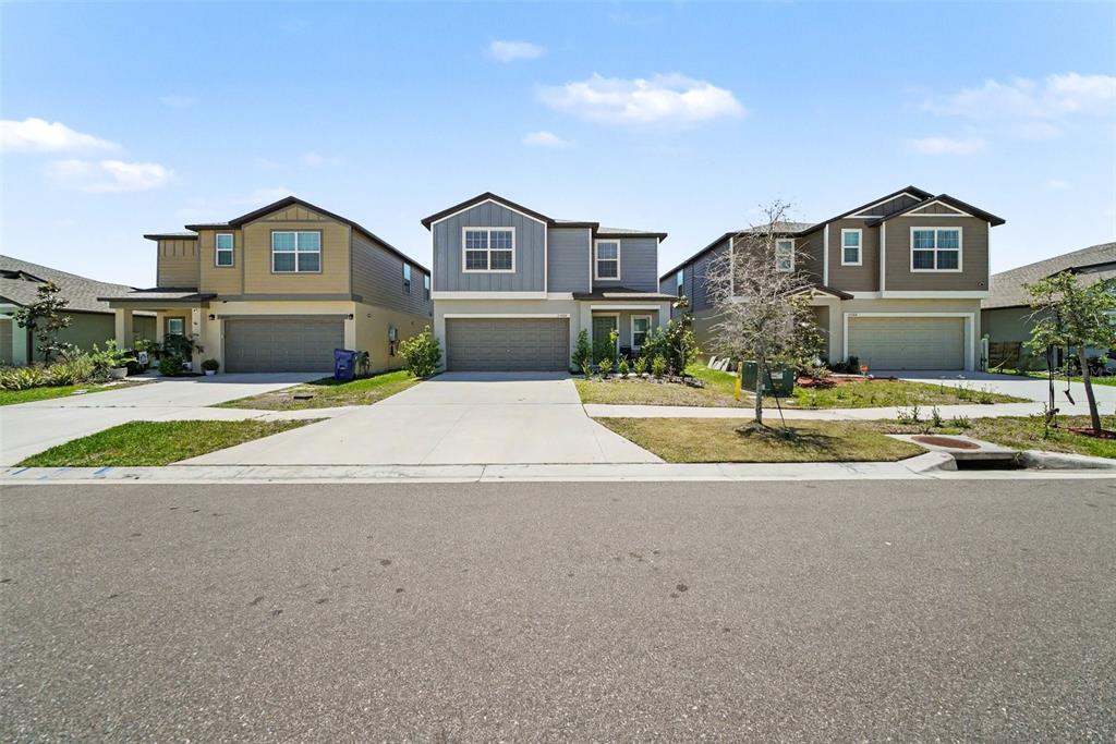 Three suburban two-story houses with driveways and garages stand side-by-side under a blue sky — 35194 ACKLEY TRCE, ZEPHYRHILLS, FL