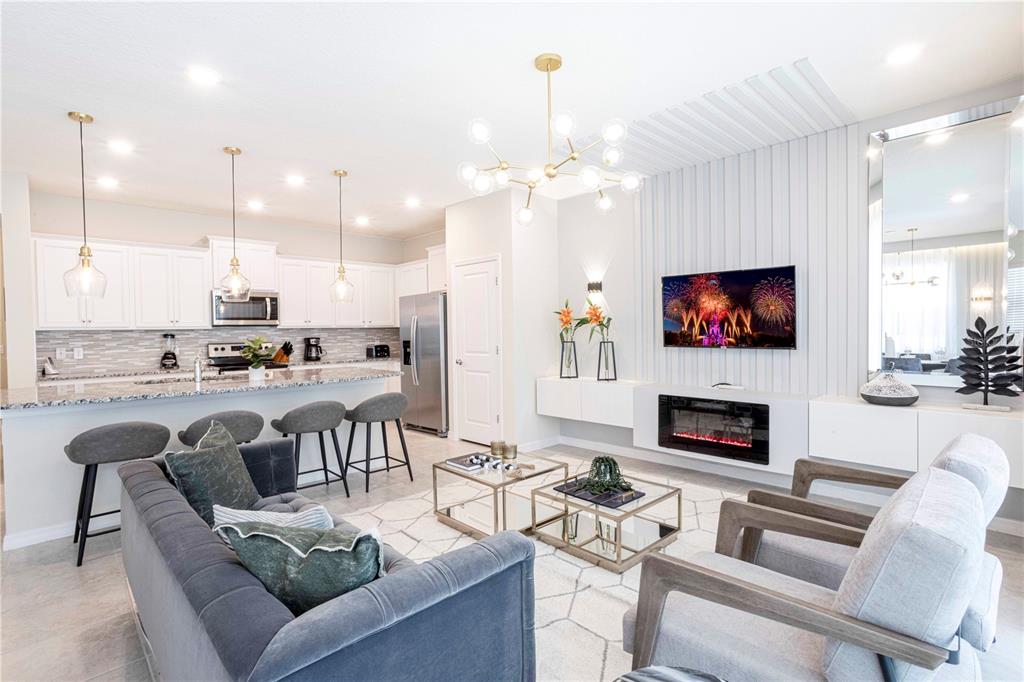 A modern open-concept living room and kitchen featuring white cabinetry, a fireplace, and gray furniture — 227 JETTY WAY, DAVENPORT, FL