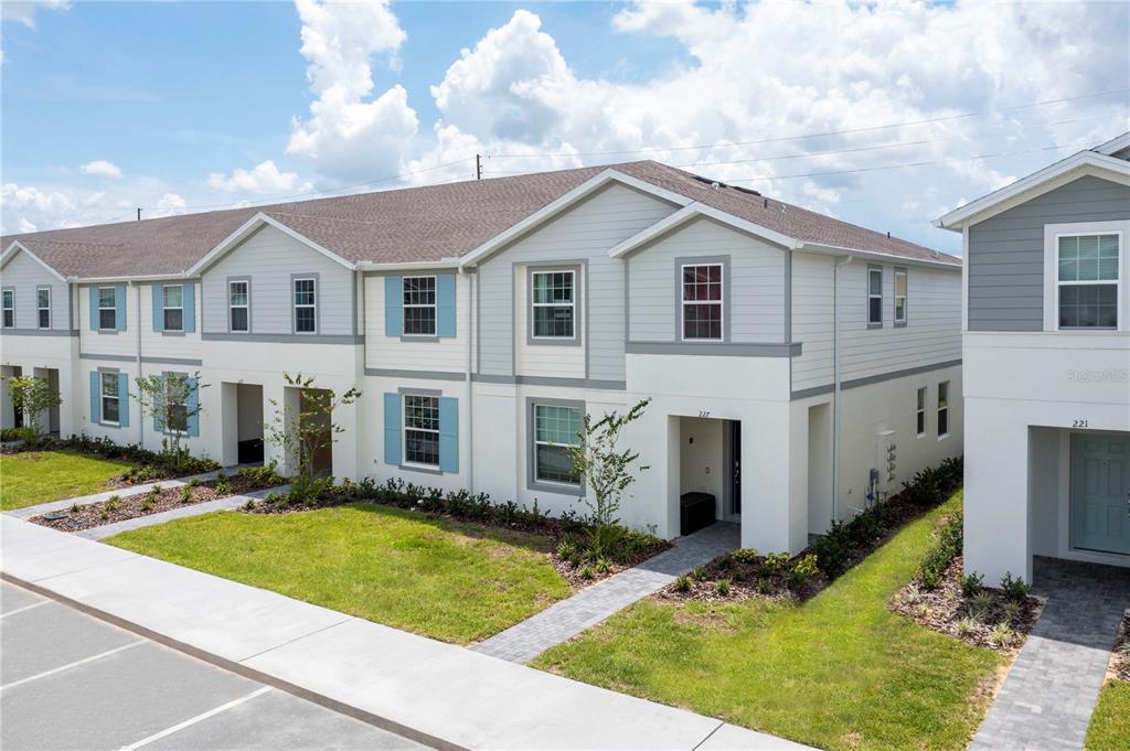 A row of two-story townhomes with light-colored siding, blue shutters, and a paved walkway — 227 JETTY WAY, DAVENPORT, FL