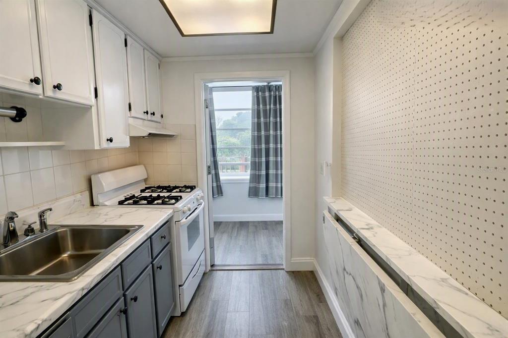 A kitchen features white upper cabinets, gray lower cabinets, a gas stove, and pegboard walls — 911 WASHINGTON AVENUE UNIT 209, LARGO, FL