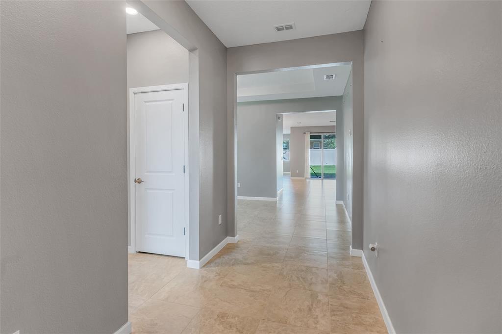 A hallway with light tile flooring leads to an open living area with sliding glass doors — 1817 LAKE SIMS PARKWAY, OCOEE, FL