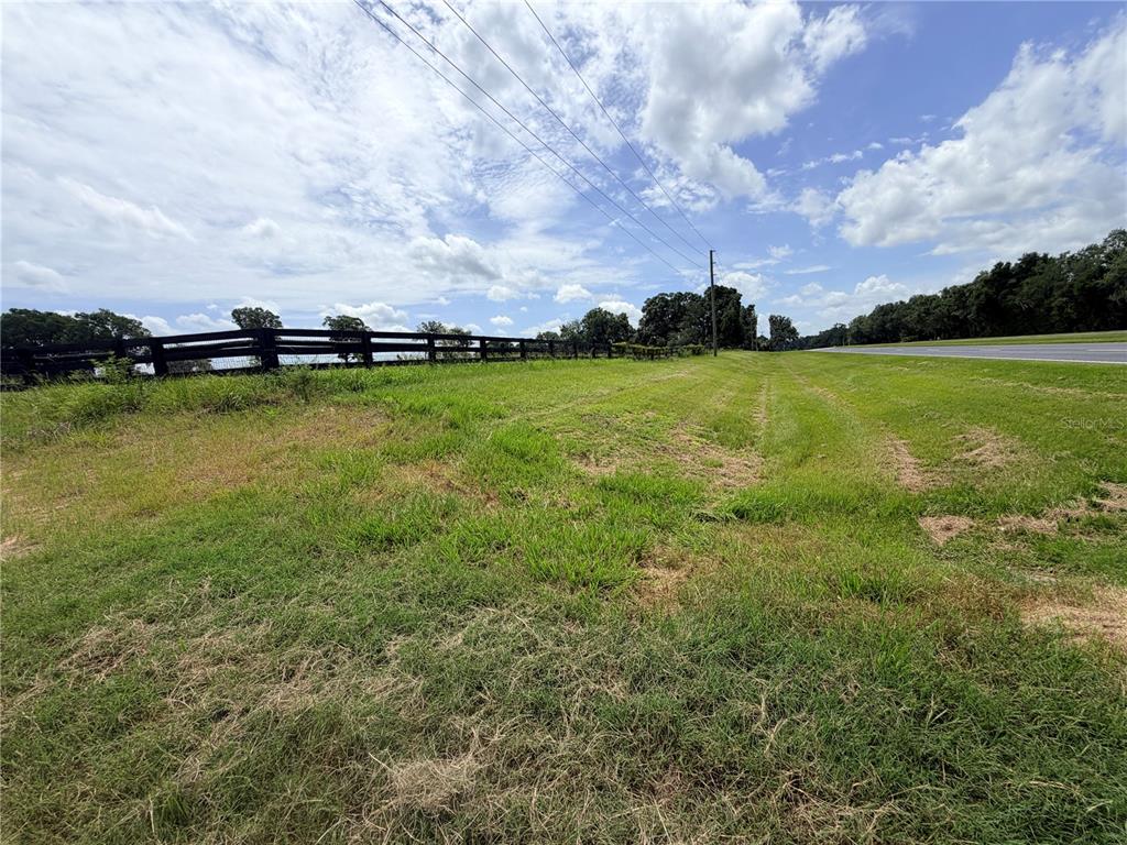 A grassy field borders a black wooden fence and a paved road under a cloudy sky — N HWY 441, CITRA, FL