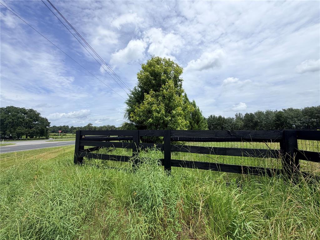 A black wooden fence borders a grassy field next to a road under a cloudy sky — N HWY 441, CITRA, FL