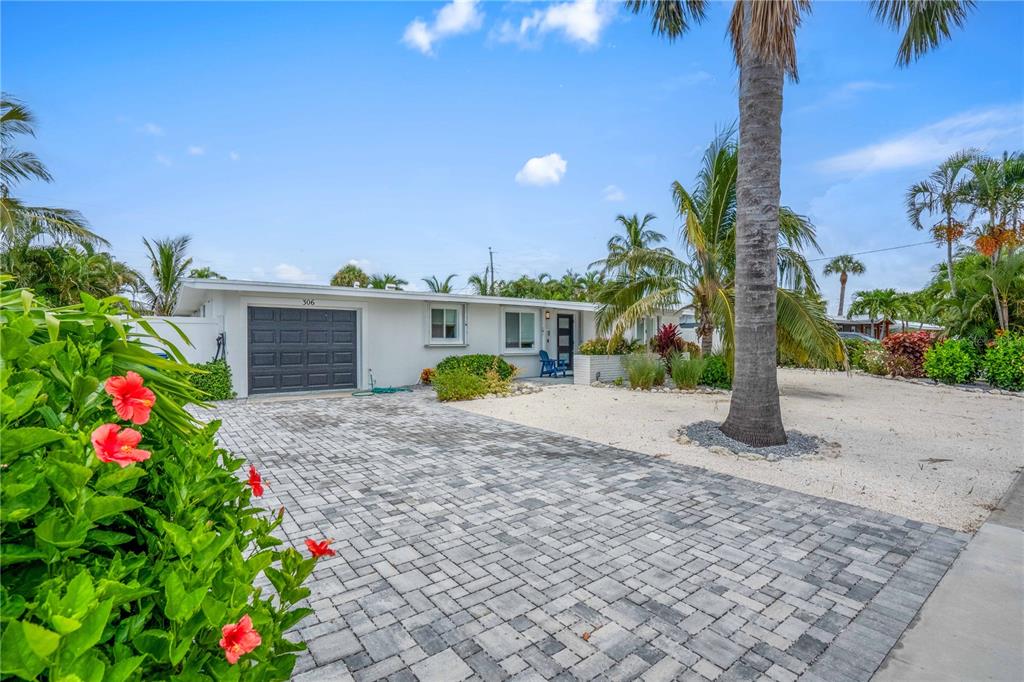 A single-story house with a paved driveway, a garage, and tropical landscaping under a blue sky — 306 66TH STREET, HOLMES BEACH, FL