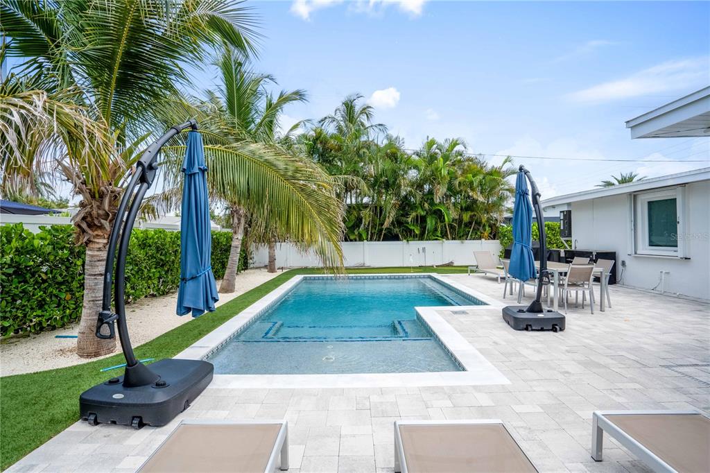 A backyard features a swimming pool with a sun shelf, patio furniture, and palm trees — 306 66TH STREET, HOLMES BEACH, FL