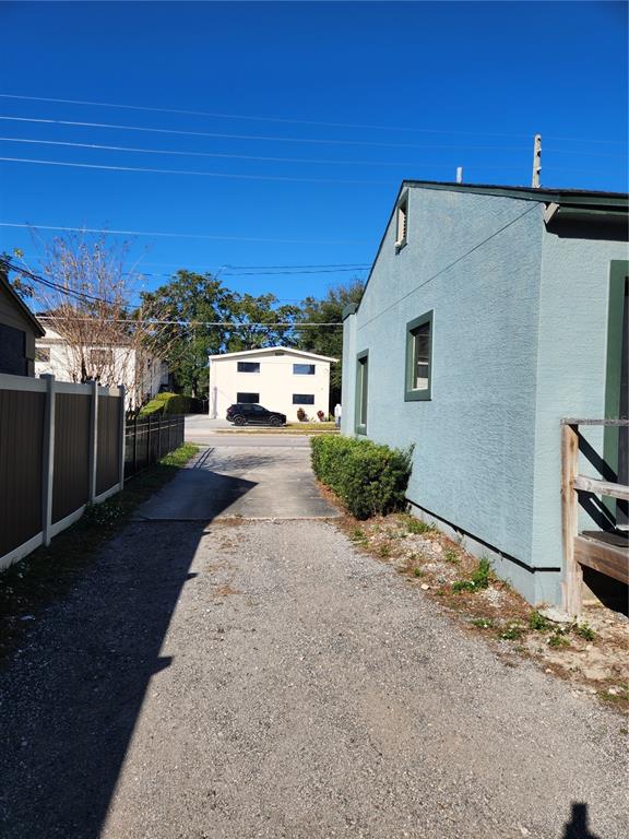 A gravel driveway leads between a light blue house and a fence toward a street — 1412 E ROBINSON STREET, ORLANDO, FL