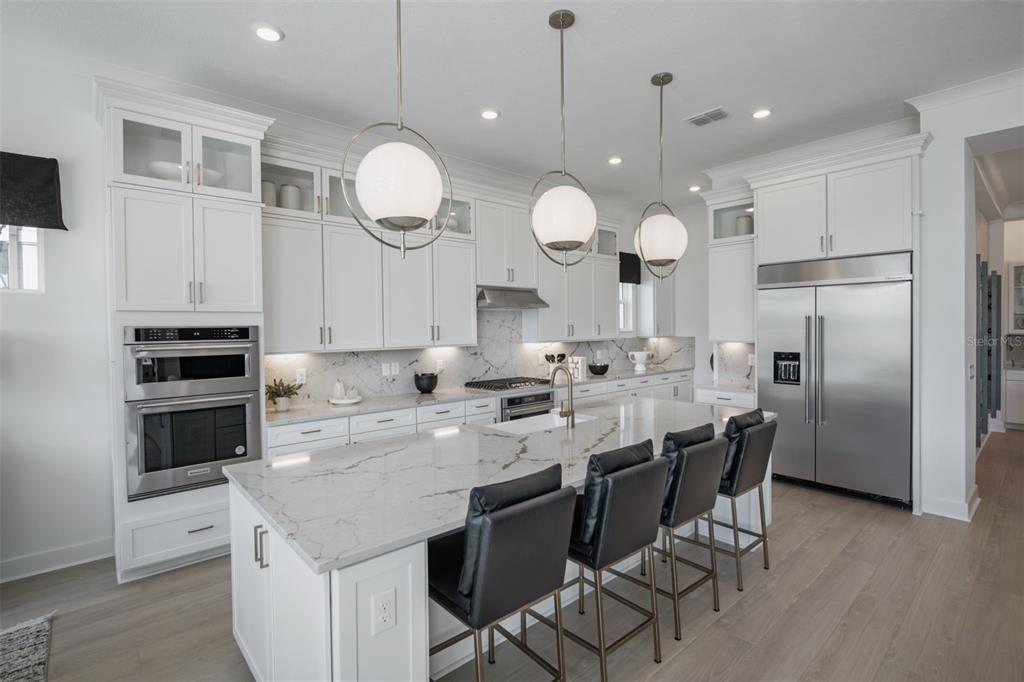 A modern white kitchen features a large marble island, stainless steel appliances, and three pendant lights — 35626 COHAGEN TRAIL, ZEPHYRHILLS, FL