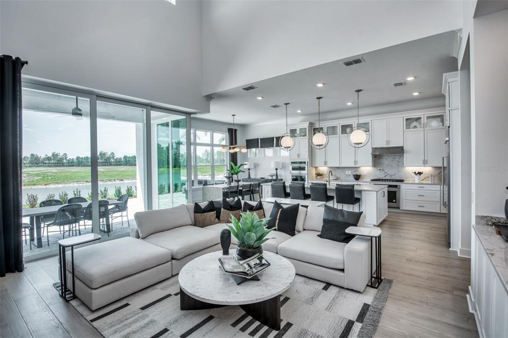A modern open-concept living room and kitchen feature high ceilings, white cabinetry, and sliding glass doors — 35626 COHAGEN TRAIL, ZEPHYRHILLS, FL