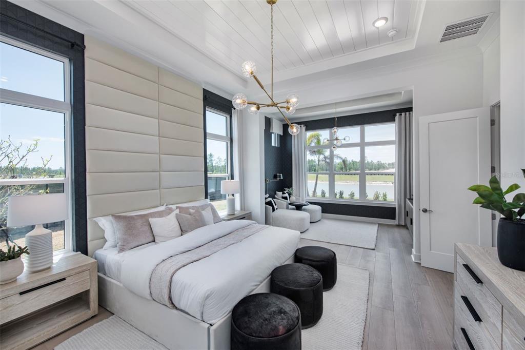 A modern bedroom features a large upholstered headboard, a central chandelier, and views of water — 35626 COHAGEN TRAIL, ZEPHYRHILLS, FL