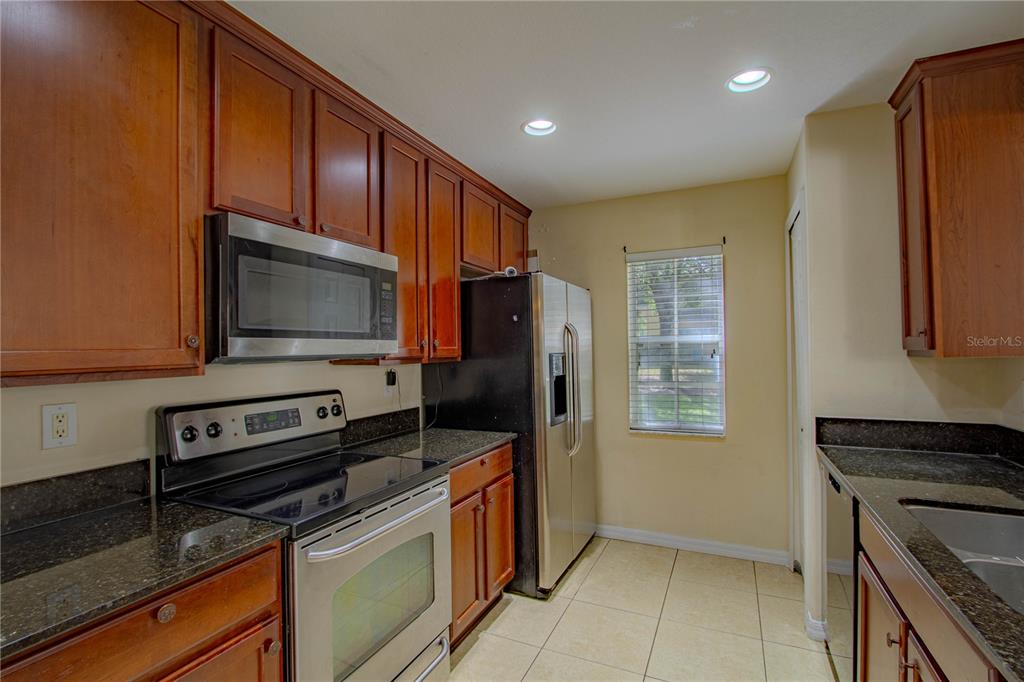 A kitchen features wood cabinets, dark granite countertops, stainless steel appliances, and tile flooring — 10917 BRICKSIDE COURT, RIVERVIEW, FL