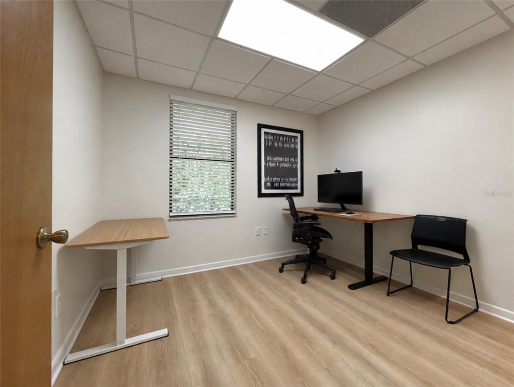 A home office features light wood-look flooring, two desks, a computer monitor, and a window — 2731 NW 41ST STREET UNIT B2, GAINESVILLE, FL