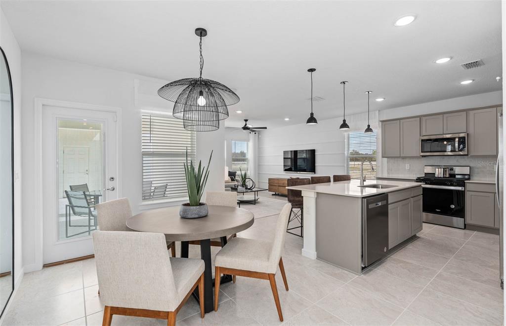 An open-concept kitchen and dining area features a round table, island, and light-colored tile flooring — 2209 SOUTHBURY DRIVE, KISSIMMEE, FL