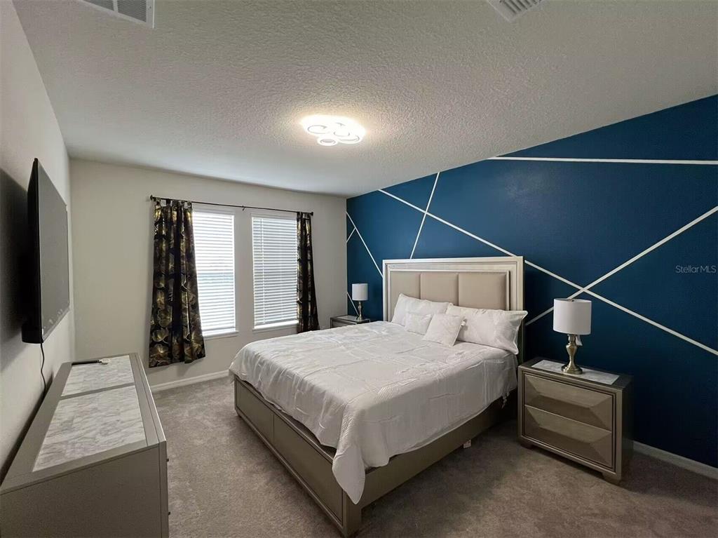 A bedroom features a blue accent wall with white geometric lines and a neutral bed — 3012 MAHALO DRIVE, DAVENPORT, FL