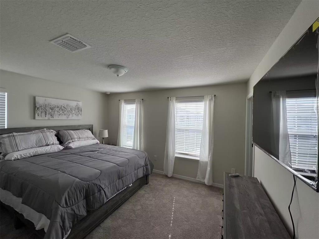 A bedroom features a large bed, a wall-mounted television, and two windows with white curtains — 3012 MAHALO DRIVE, DAVENPORT, FL
