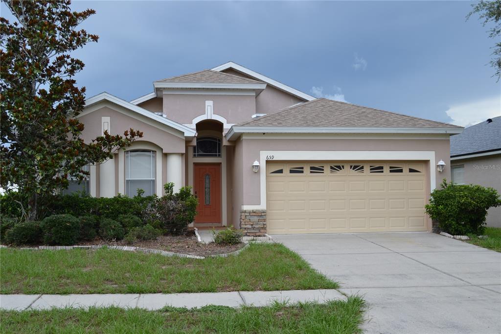 A single-story house with a beige stucco exterior, a two-car garage, and a concrete driveway — 659 WINTHROP DRIVE, SPRING HILL, FL