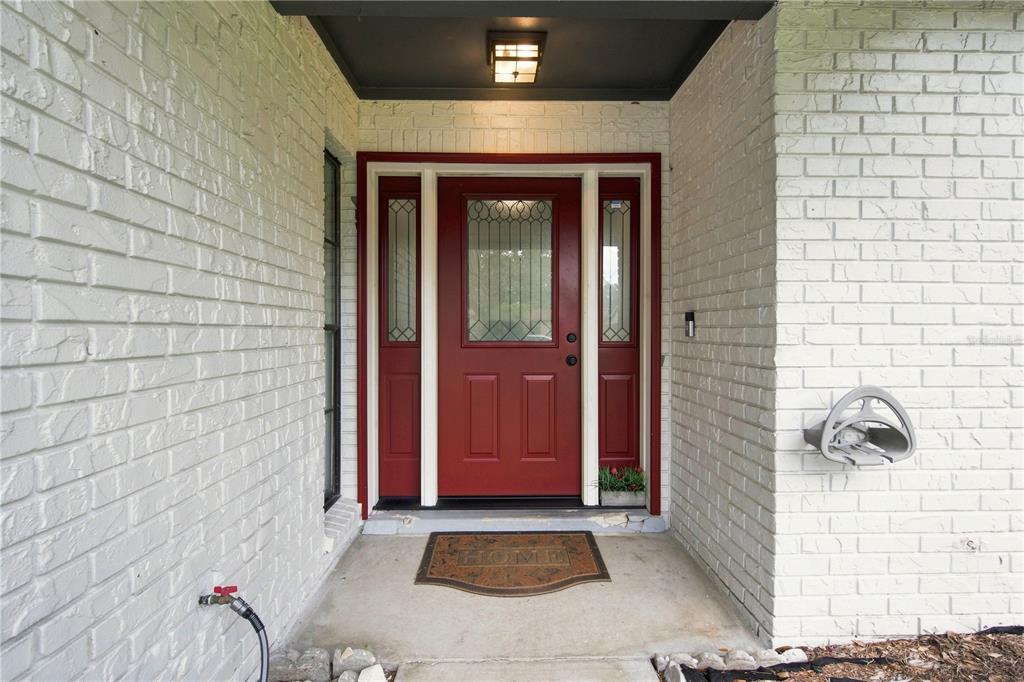 A red front door with sidelights is set into a white painted brick exterior wall — 4313 FOXGLEN LANE, TAMPA, FL
