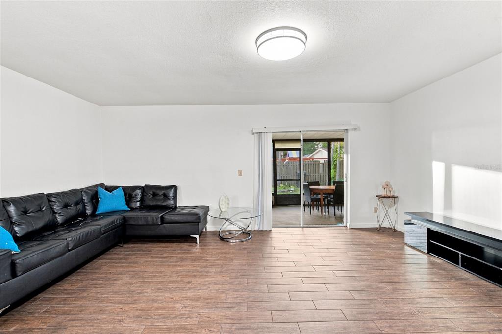 A living room features a black sectional sofa, wood-look tile flooring, and a sliding glass door — 4313 FOXGLEN LANE, TAMPA, FL
