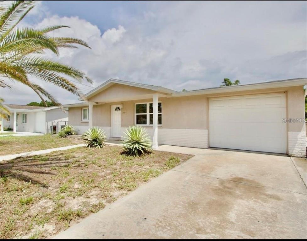A single-story house with a beige exterior, white brick base, and an attached garage — 7407 UNIVERSITY DRIVE, HUDSON, FL