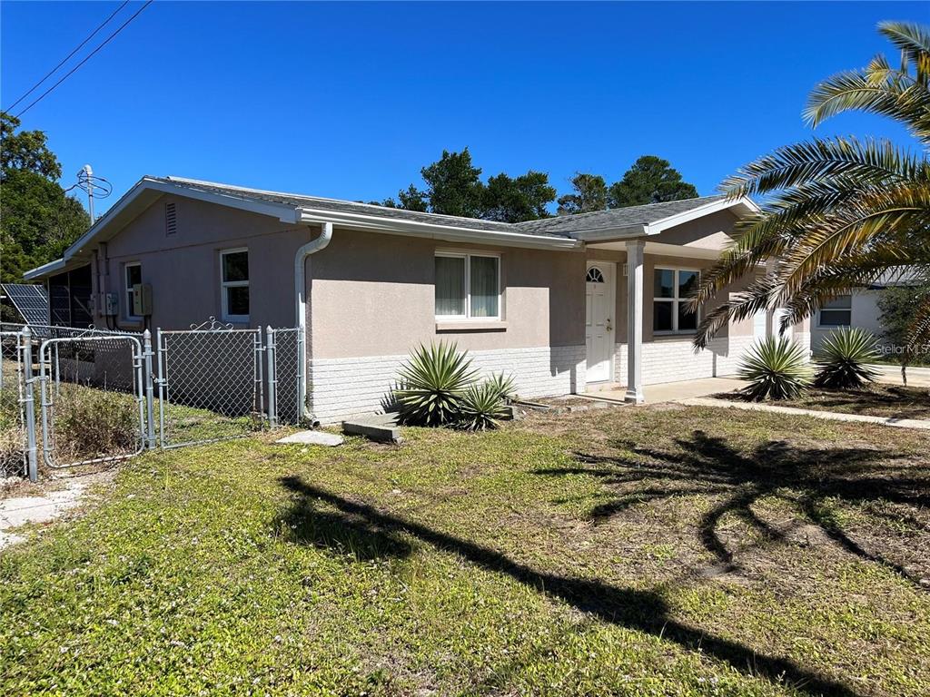 A single-story house with a light-colored stucco exterior and a chain-link fence — 7407 UNIVERSITY DRIVE, HUDSON, FL
