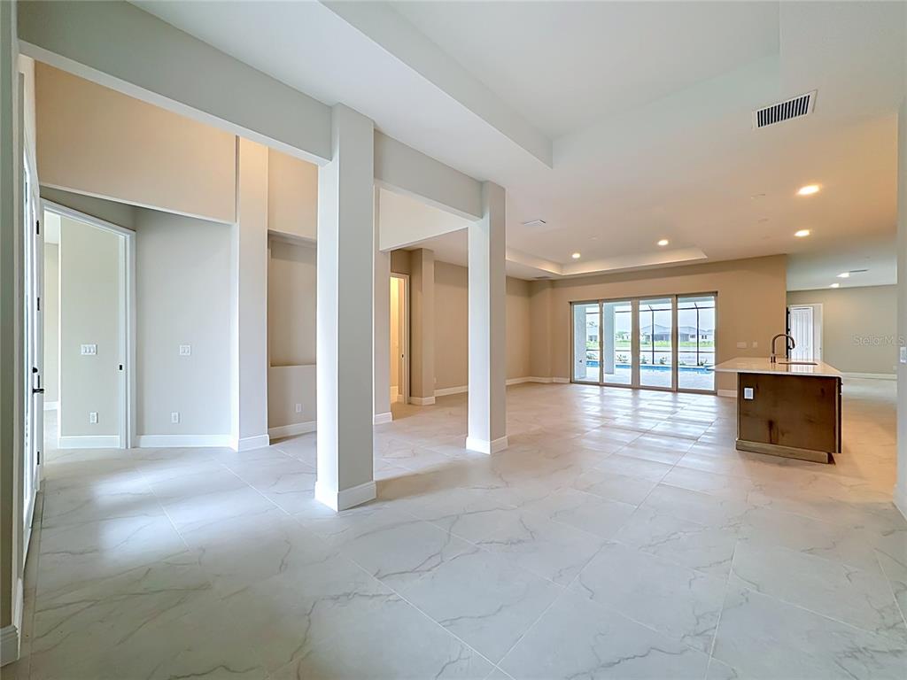 An open-concept living area features large white floor tiles, support columns, and a kitchen island — 12418 STONEGATE TRAIL, PARRISH, FL