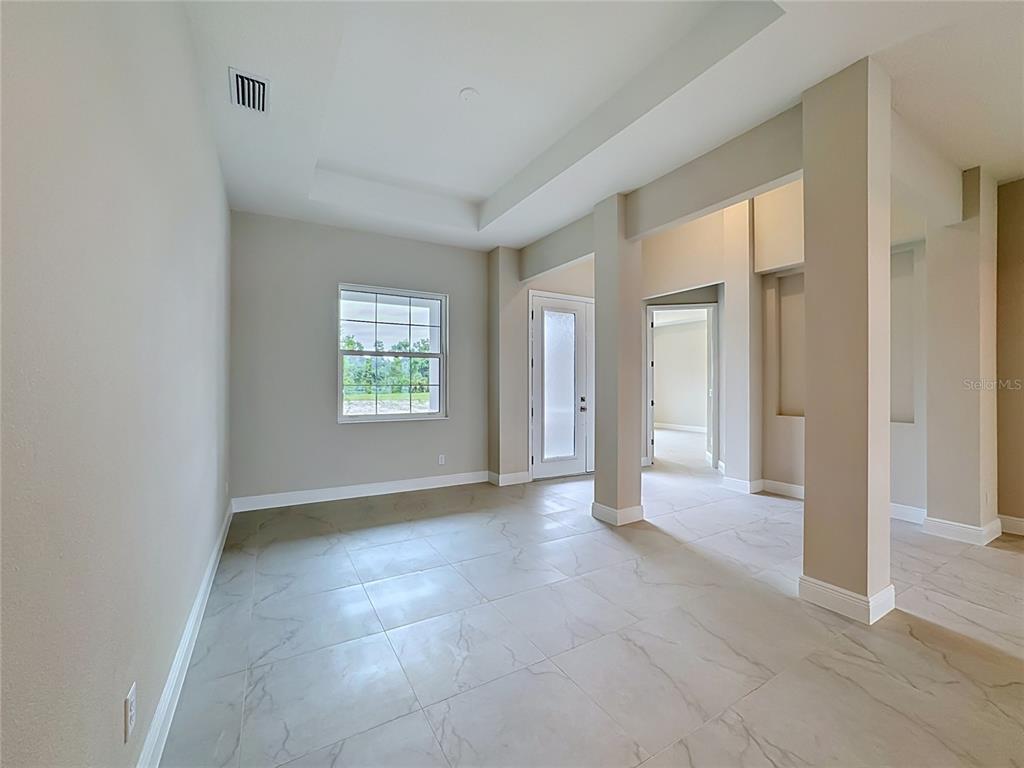 An empty room with light-colored tile flooring, a tray ceiling, and a glass-paneled door — 12418 STONEGATE TRAIL, PARRISH, FL