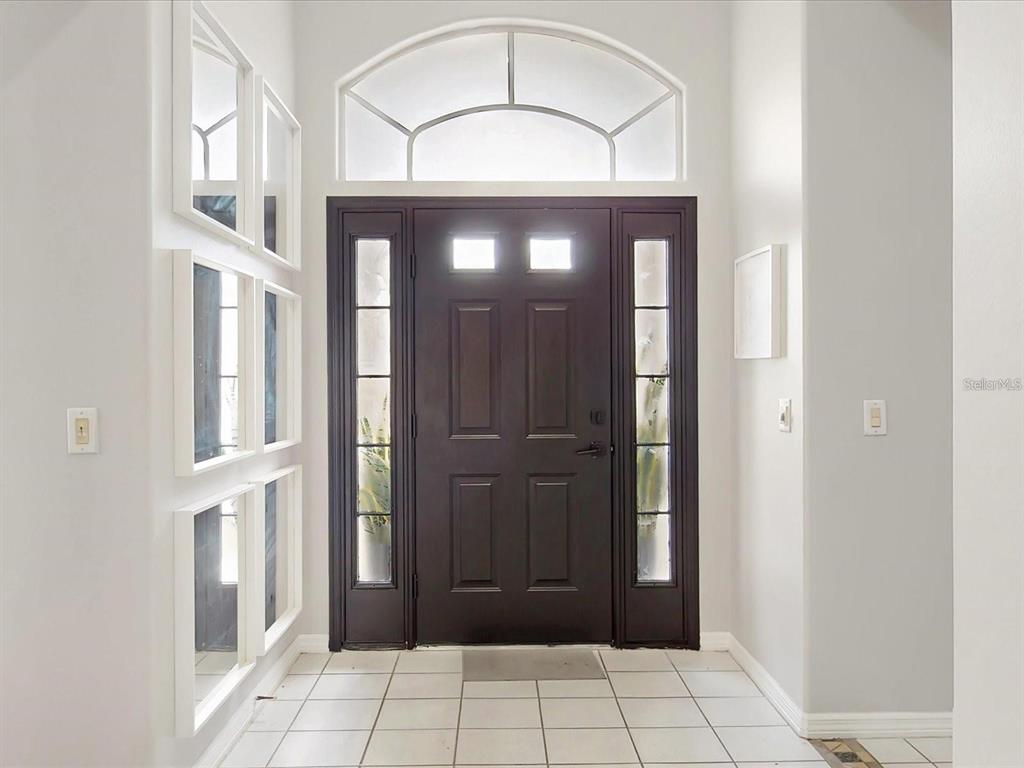 An entryway features a dark front door with sidelights, a transom window, and tiled flooring — 1718 GOLFVIEW DRIVE, KISSIMMEE, FL