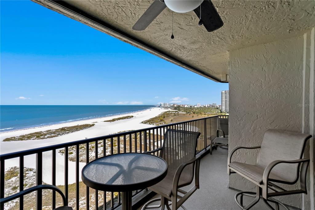 An aerial view shows a tall beachfront condominium building with a parking lot and pool — 1290 GULF BOULEVARD UNIT 1002, CLEARWATER, FL