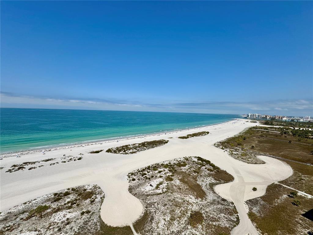 An aerial view shows high-rise condominiums situated along a sandy beach and the ocean — 1290 GULF BOULEVARD UNIT 1002, CLEARWATER, FL