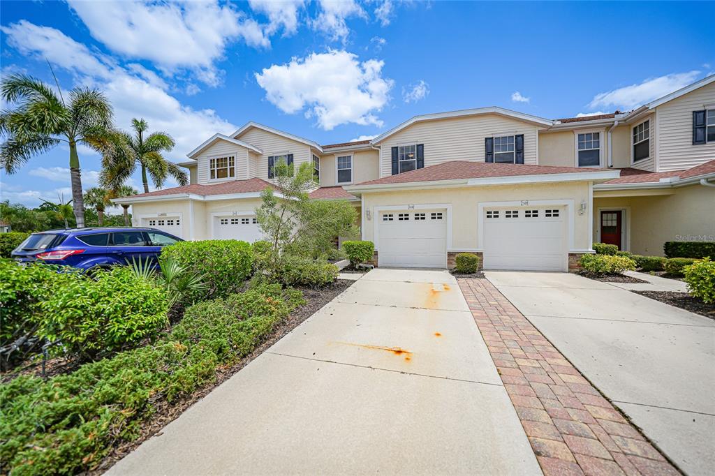 A multi-unit residential building with beige siding, white garage doors, and a paved driveway — 2330 FELICITY PLACE, NORTH PORT, FL