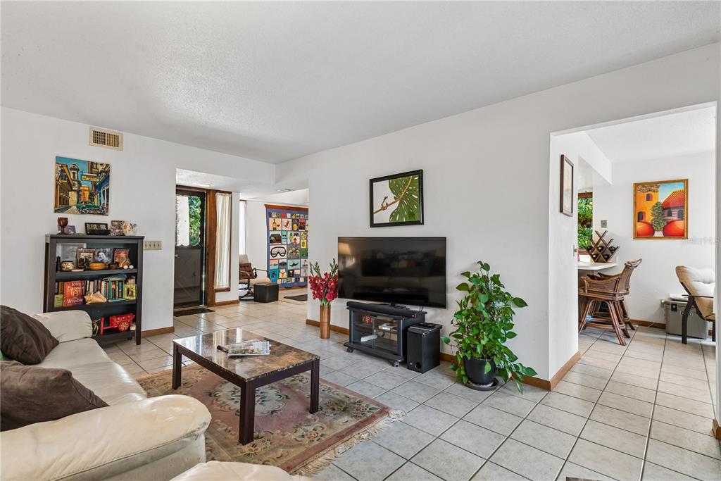 A living room with tile floors, a television, a bookshelf, and an adjacent dining area — 13 PINEHURST PLACE UNIT 13, PALM COAST, FL