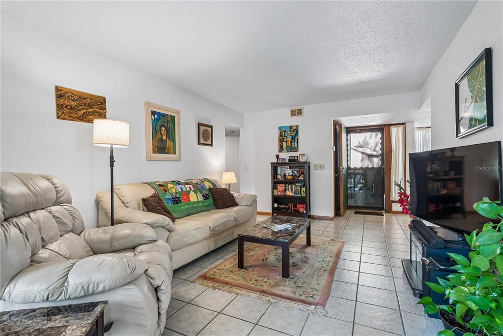A living room features a beige sofa, a recliner, a coffee table, and tile flooring — 13 PINEHURST PLACE UNIT 13, PALM COAST, FL